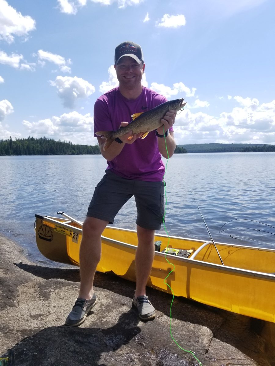 Keith Ramsett holding a lake trout beside a canoe in the Boundary Waters